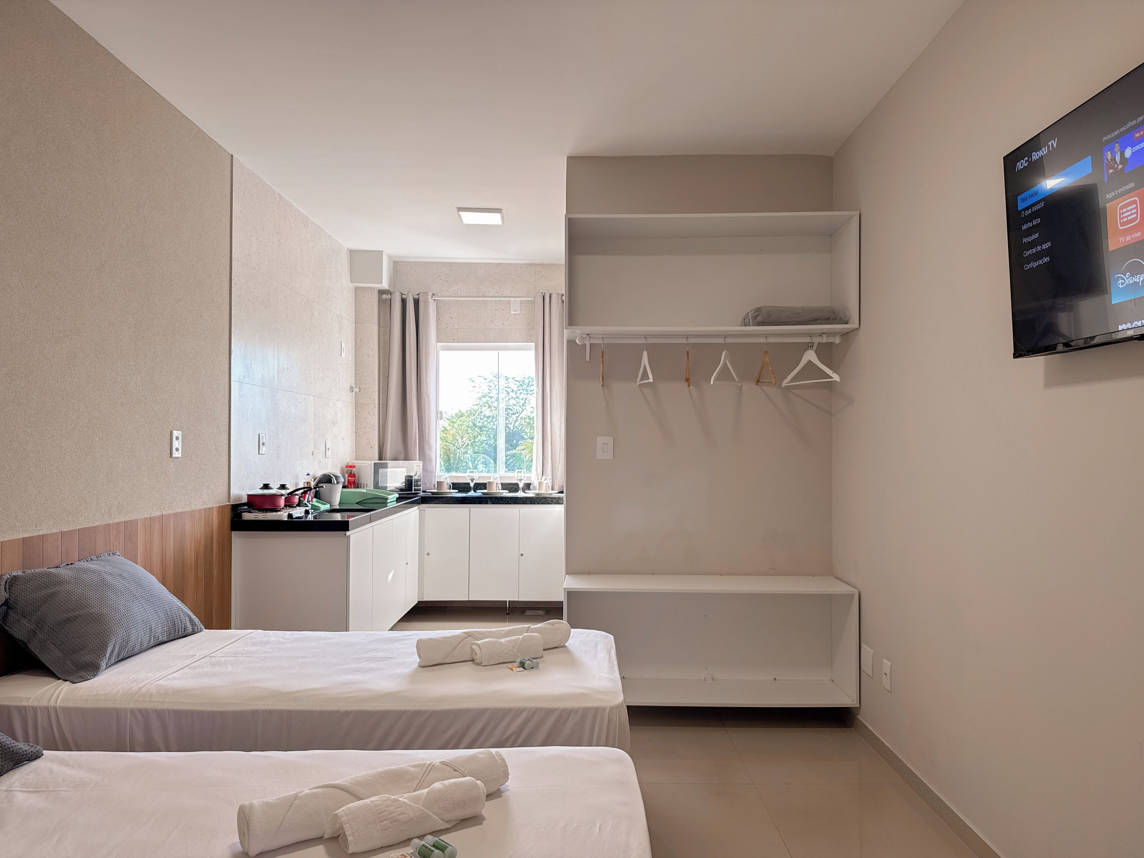 A hotel room with two beds, a kitchenette, a wardrobe, and a TV mounted on the wall.
