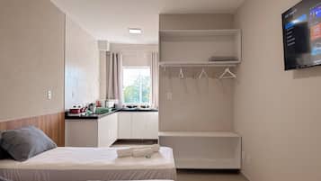 A hotel room with two beds, a kitchenette, a wardrobe, and a TV mounted on the wall.