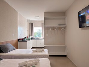 Une chambre d’hôtel avec deux lits, une kitchenette, une armoire et un téléviseur fixé au mur.
