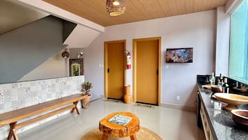 A modern kitchen with a wooden bench, a woven stool, and a television on the wall.