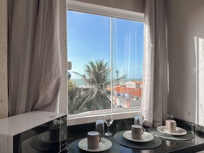 Una habitación con vista al mar, una mesa de comedor con platos, vasos y una taza, además de un microondas en la encimera.