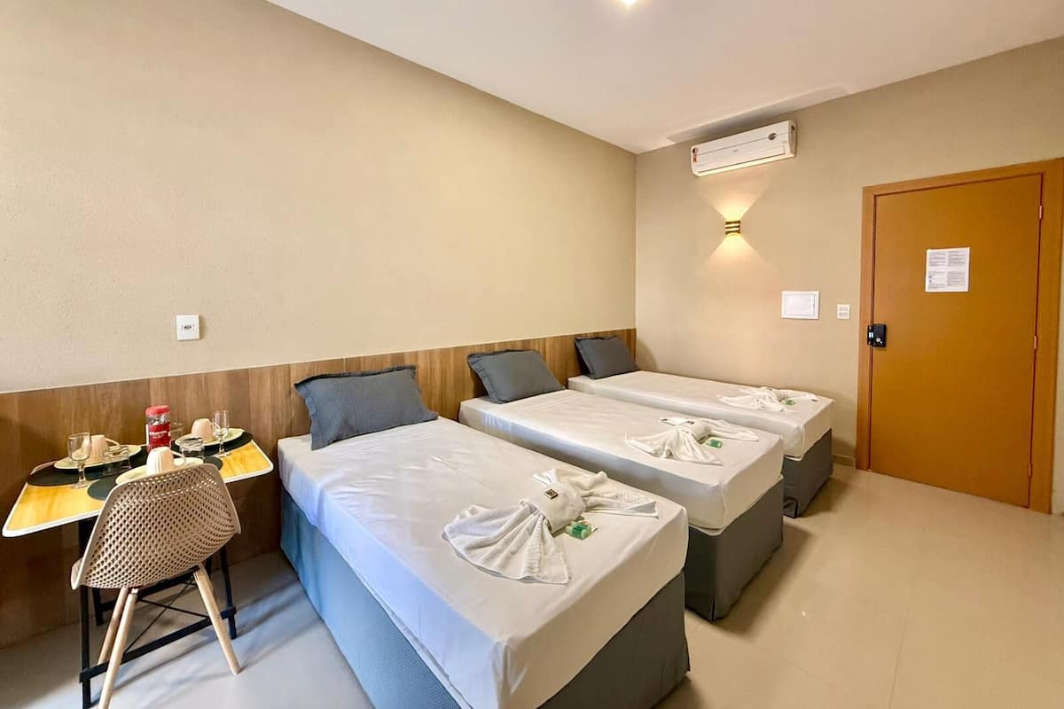 Ein Hotelzimmer mit zwei Einzelbetten, einem kleinen Schreibtisch mit Stuhl und einer Wand-Klimaanlage.