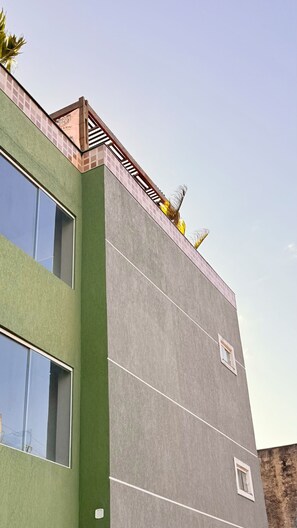 Een meerhoog gebouw met een groene gevel, grote ramen en een plat dak met een klein balkon.