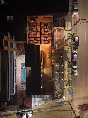 An aerial view of a hotel with a pool, a wooden deck, and a parking area with cars.