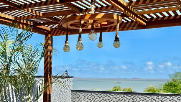 An outdoor patio with wooden furniture and hanging light fixtures, overlooking a body of water. - Your Home - Studios Boutique Hotel (Sao Luis)