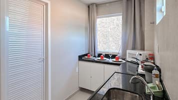 Cozinha compacta com micro-ondas embutido, pia com tapete verde e janela com cortinas.