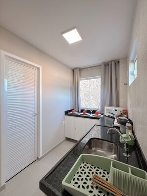 Una cocina compacta con microondas integrado, un lavamanos con felpudo verde y una ventana con cortinas.