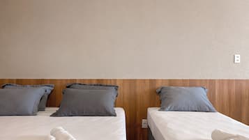 A hotel room with two beds, each with a white mattress and grey pillows. There are rolled white towels on the beds.