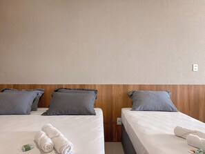 Habitación de hotel con dos camas, cada una con colchón blanco y almohadas grises. Hay toallas blancas dobladas sobre las camas.
