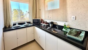 A compact kitchen with a window, a microwave, a sink, and a dish drying rack. - Your Home - Studios Boutique Hotel (Sao Luis)