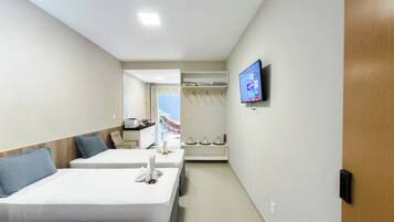 Quarto de hotel com duas camas, televisão, guarda-roupa e vista para o mar.