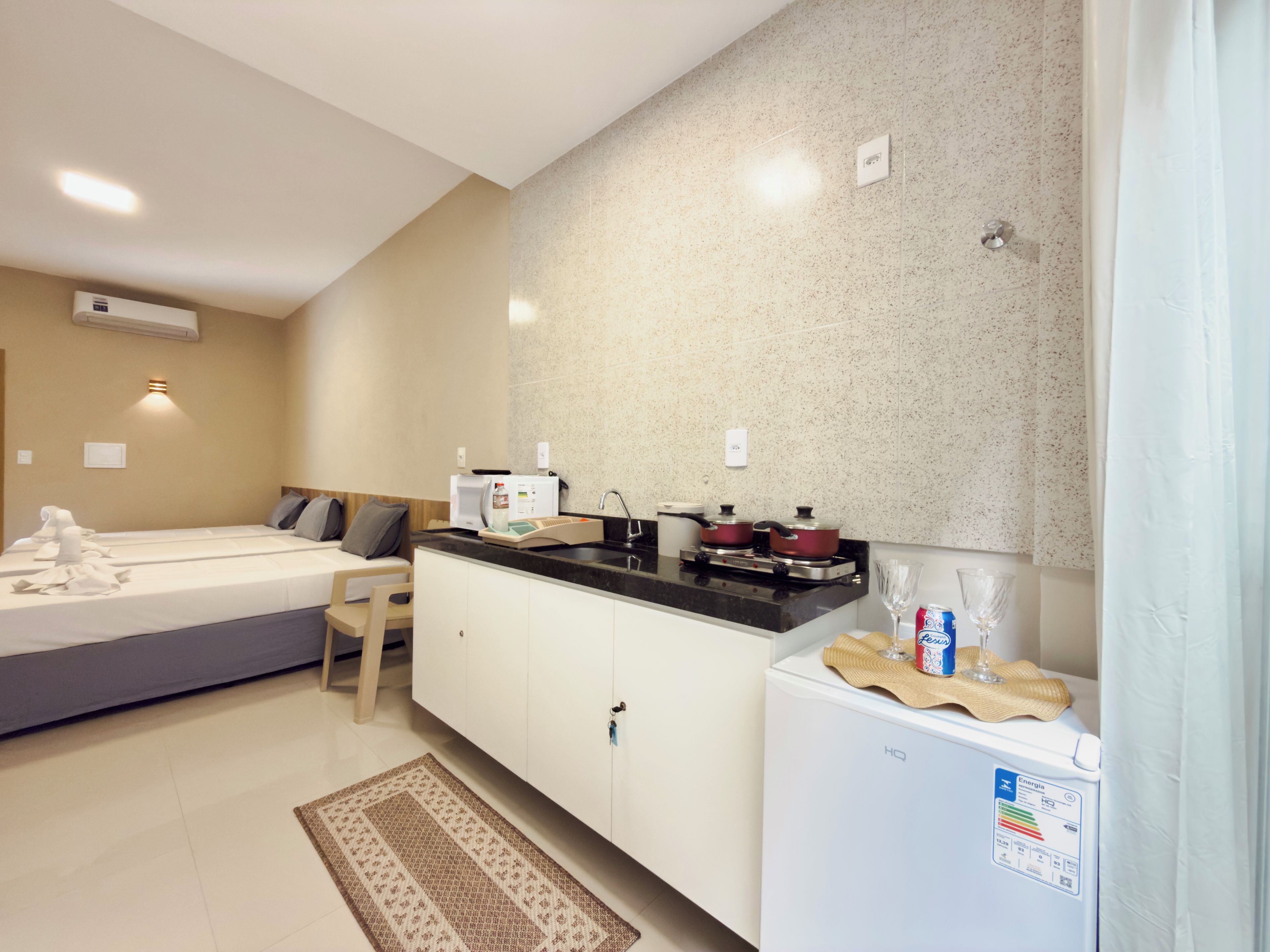 A modern hotel room with a kitchenette, a bed with towels, a small seating area, and a refrigerator.