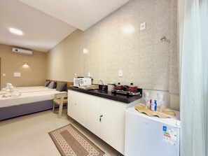 Een moderne hotelkamer met kitchenette, een bed met handdoeken, een zithoekje en een koelkast.