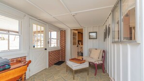 A cozy room with a wooden bench, a cushioned chair, a patterned rug, and a brick wall.