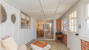 A cozy room with a sofa, a small table, and a patterned floor. There is a sliding glass door leading to a dining area with chairs and a table.