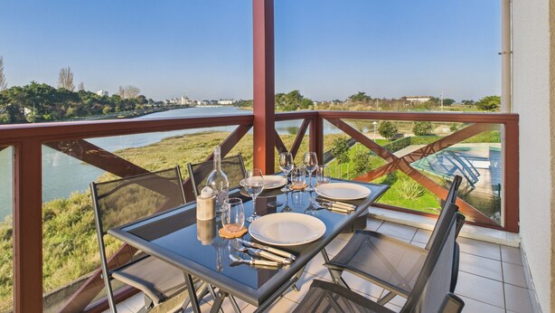 A dining table set outdoors with a view of a river and distant buildings. - Apartment - balcony with view - swimming pool (Guérande)