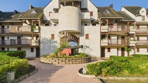 A multi-story hotel with a central cylindrical tower, balconies, and a landscaped courtyard. - Apartment - balcony with view - swimming pool (Guérande)