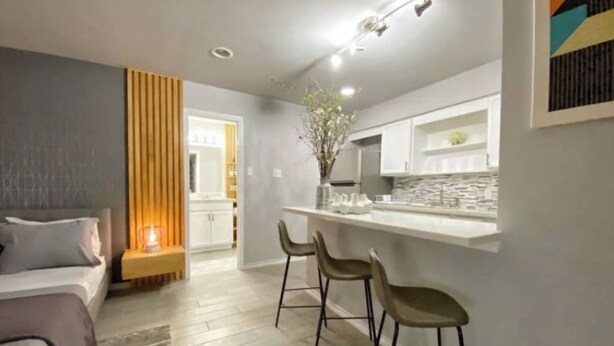 A modern apartment with a kitchenette, a dining area with bar stools, a bed, and a large window. - Montrose Cheery Studio! Medical Center 09 ★★★★★ (Houston)