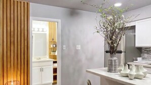 A modern kitchen with white cabinets, a wooden accent wall, and a vase with branches. - Montrose Cheery Studio! Medical Center 09 ★★★★★ (Houston)