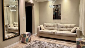 Un salon avec un canapé beige, un grand miroir, un lustre et une œuvre d’art encadrée accrochée au mur.