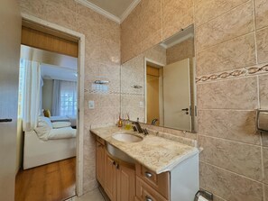 Une salle de bain avec un lavabo en marbre, des meubles en bois, un grand miroir et une porte donnant sur une chambre.