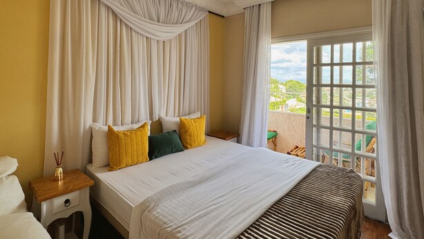 Une chambre avec un grand lit, des rideaux blancs et une vue sur la verdure.