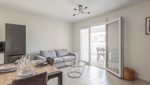 Een moderne woonkamer met een eethoek, een bank, een glazen tafel en een schuifpui naar een buitenbalkon.