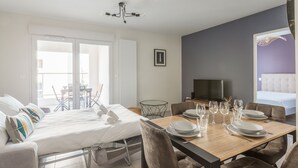 Een moderne eetruimte met een houten tafel gedekt voor vier personen, een bank met een gestreept kussen en een televisie op de achtergrond.