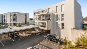Een modern, meerhoog gebouw met een overdekte parkeerruimte en een zwarte auto die er geparkeerd staat.