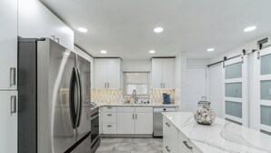 Una cocina moderna con armarios blancos, un refrigerador de acero inoxidable, horno empotrado y encimera de mármol.