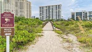 Un sendero que conduce a una playa, con un letrero que indica propiedad privada y acceso a la playa.