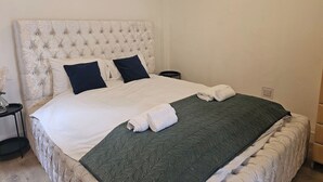 A neatly made bed with a tufted headboard, two pillows, a green quilt, and a rolled towel. - Cosy Studio in the Heart of Bridgend (Bridgend County Borough)