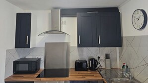A modern kitchen with dark cabinets, a microwave, a toaster, a kettle, and a sink. - Cosy Studio in the Heart of Bridgend (Bridgend County Borough)