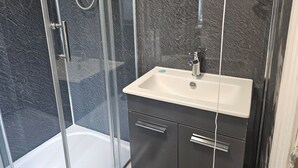 A bathroom with a glass-enclosed shower, a white sink, and dark-toned cabinets. - Cosy Studio in the Heart of Bridgend (Bridgend County Borough)