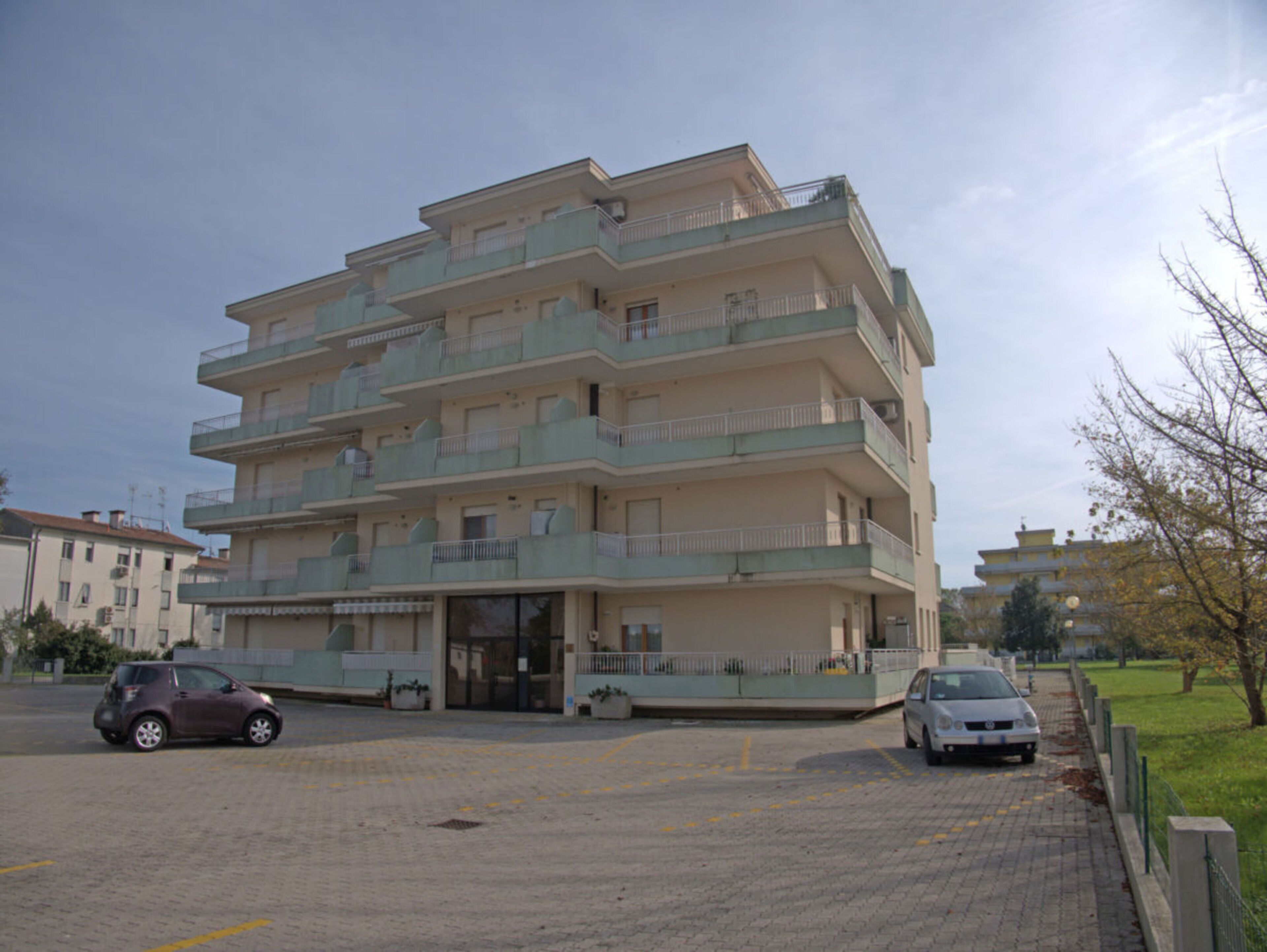 A multi-story residential building with balconies, a parking area, and a gated entrance.