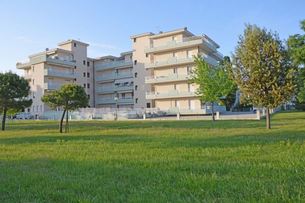 A multi-story residential building with balconies, surrounded by a grassy area and trees. - Cozy Studio With Pool in Caorle (Caorle)