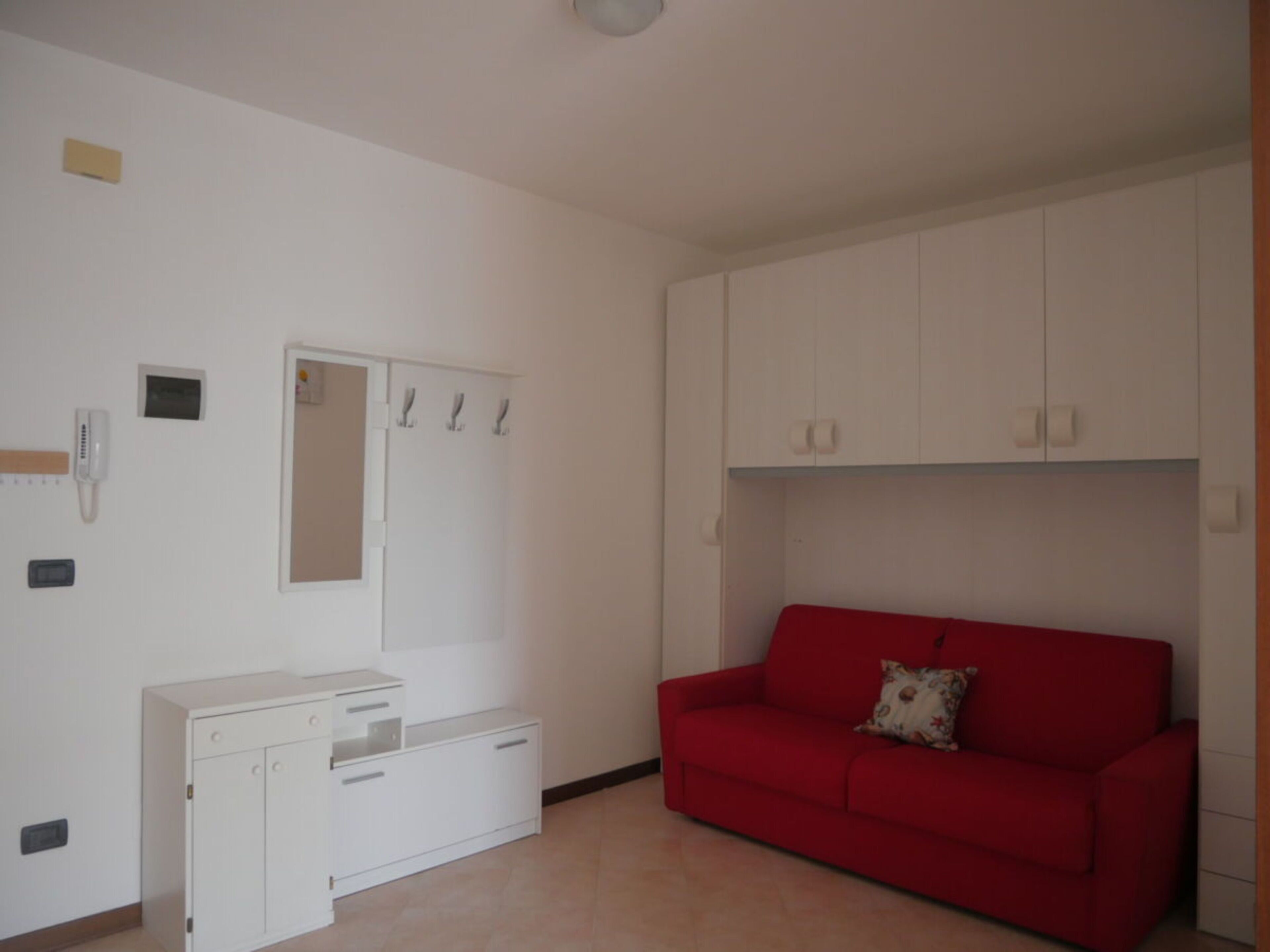 A room with a red sofa, white wardrobe, and a small desk.