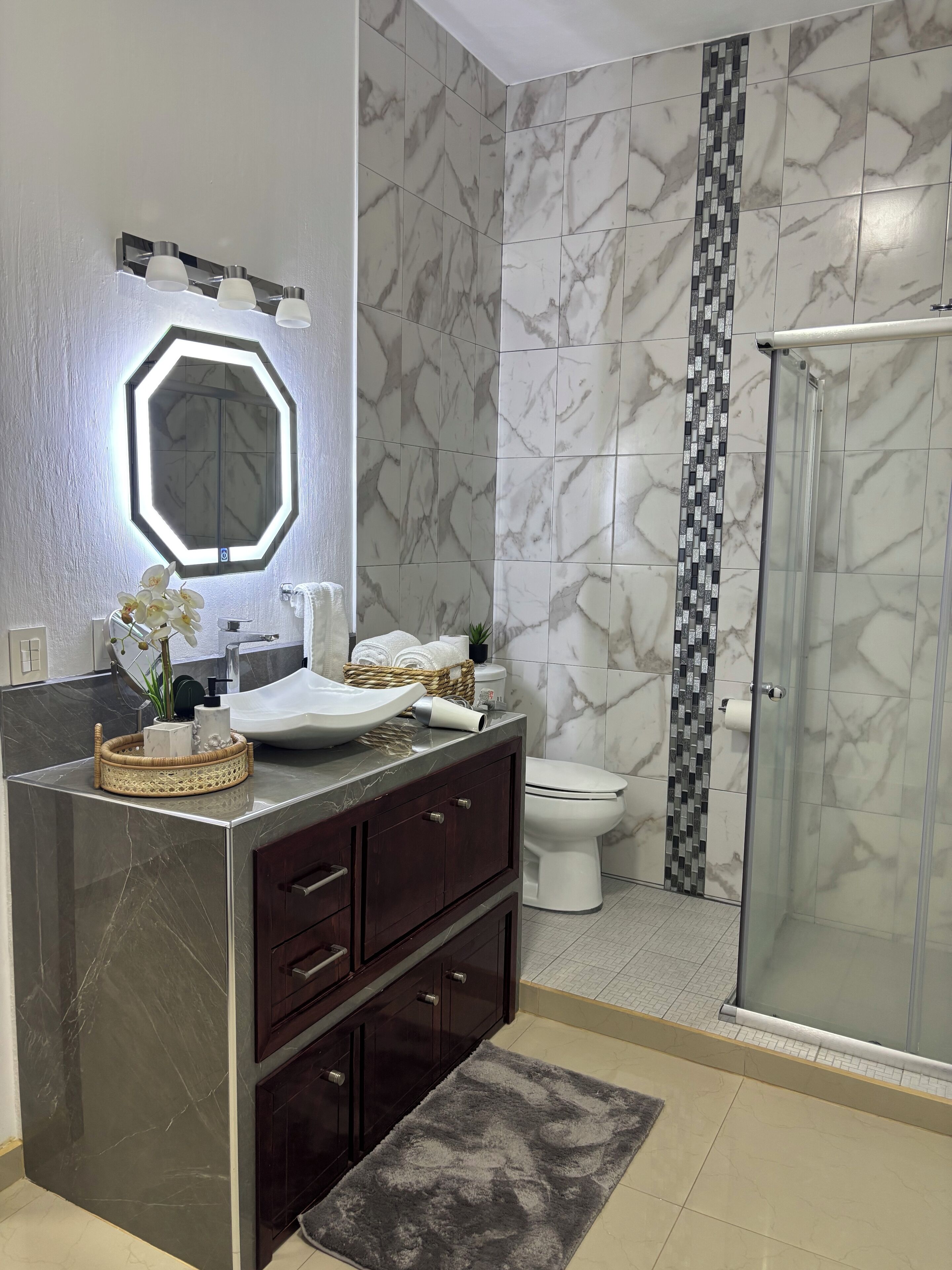 Un baño moderno con tocador de mármol, un espejo grande, cabina de ducha y un inodoro.