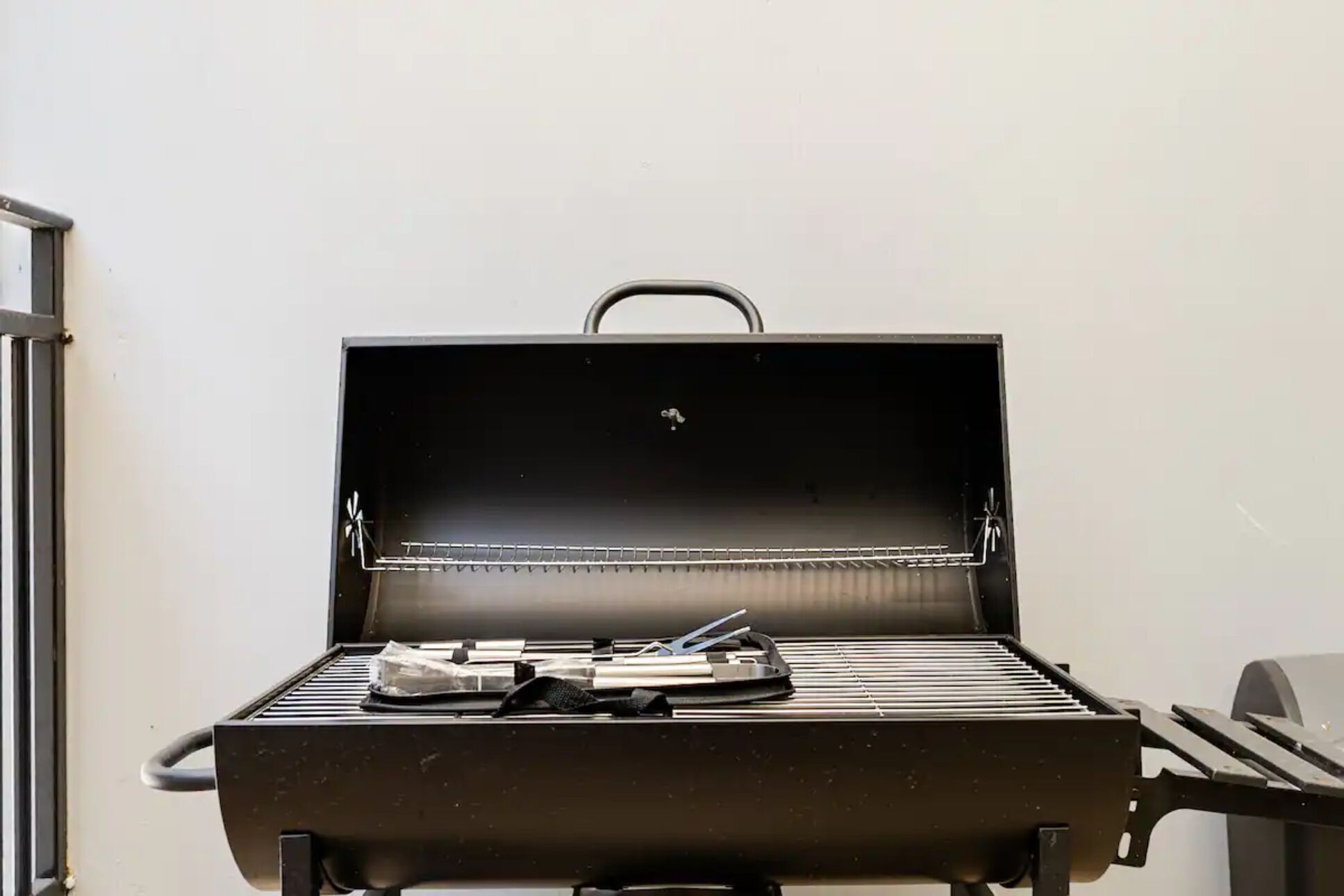 An open grill with a handle, a metal rack, and some utensils on the grill surface.