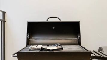 An open grill with a handle, a metal rack, and some utensils on the grill surface.