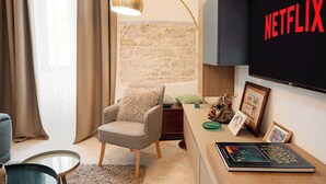 A modern living room with a stone wall, a comfortable armchair, a desk with a book, and a TV displaying "NETFLIX". - Ex Monastero in Centro Storico a Bitetto, 3 Bedrooms, Free Wi-Fi. (Bitetto)