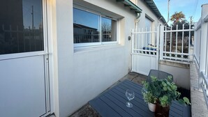 Una casa amb façana blanca, una finestra i un petit pati amb una taula i una planta en test.
