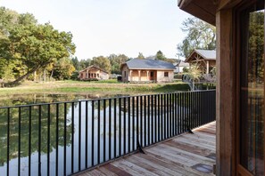 A wooden deck with a metal railing overlooking a body of water and houses in the background. - Woodland Cabin in Vencimont (Gedinne)