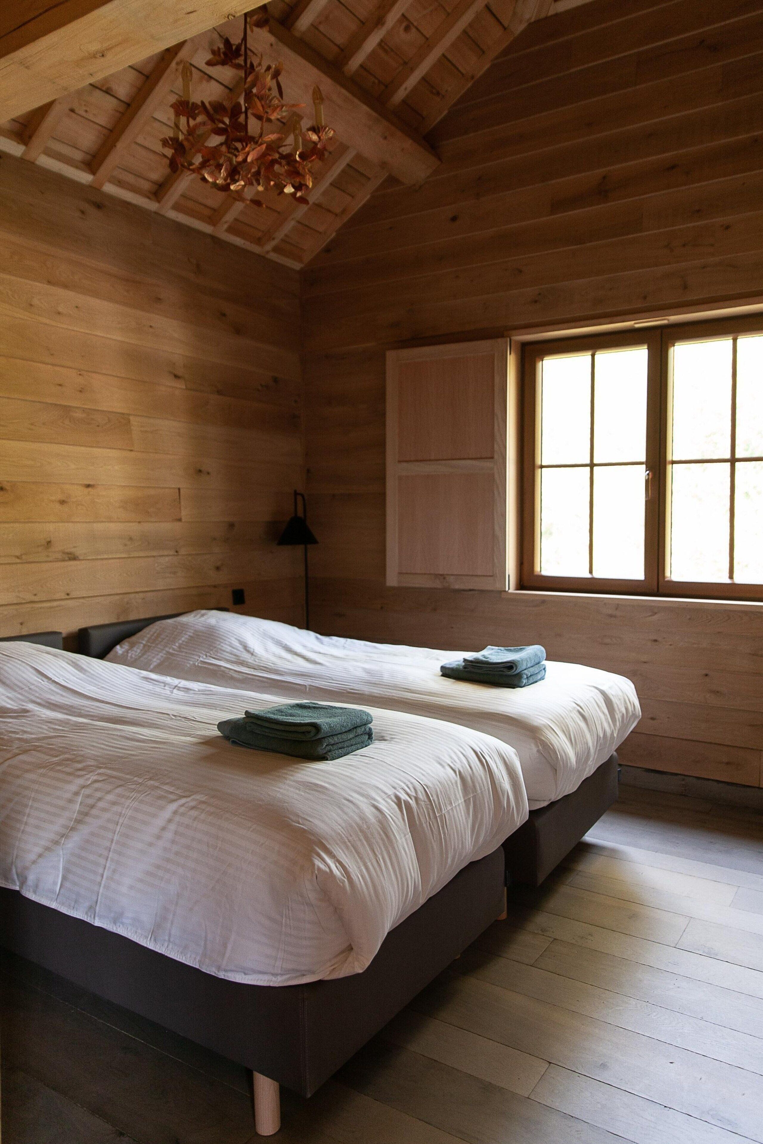 Een houten slaapkamer met twee bedden, een raam en een hanglamp.