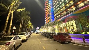 A multi-story hotel with balconies, a parking lot, and palm trees along the street. - Hotel Sea View (Hoang Tien)