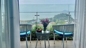 A balcony with two wicker chairs and a small table, a vase with flowers, and a view of the sea and distant hills. - Hotel Sea View (Hoang Tien)