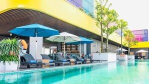 A pool area with lounge chairs and umbrellas, a bar area with seating, and a modern building with a curved roof. - Hotel Sea View (Hoang Tien)