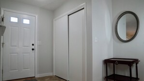 Ein Flur mit einer weißen Tür, einem geschlossenen Schrank und einem kleinen Holztischchen mit Spiegel.