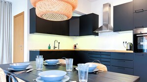 Eine moderne Küche mit dunklen Schränken, einem Holzespeisetisch mit Schüsseln und Gläsern, einer hängenden orangefarbenen Leuchte und einem Edelstahlbackofen.