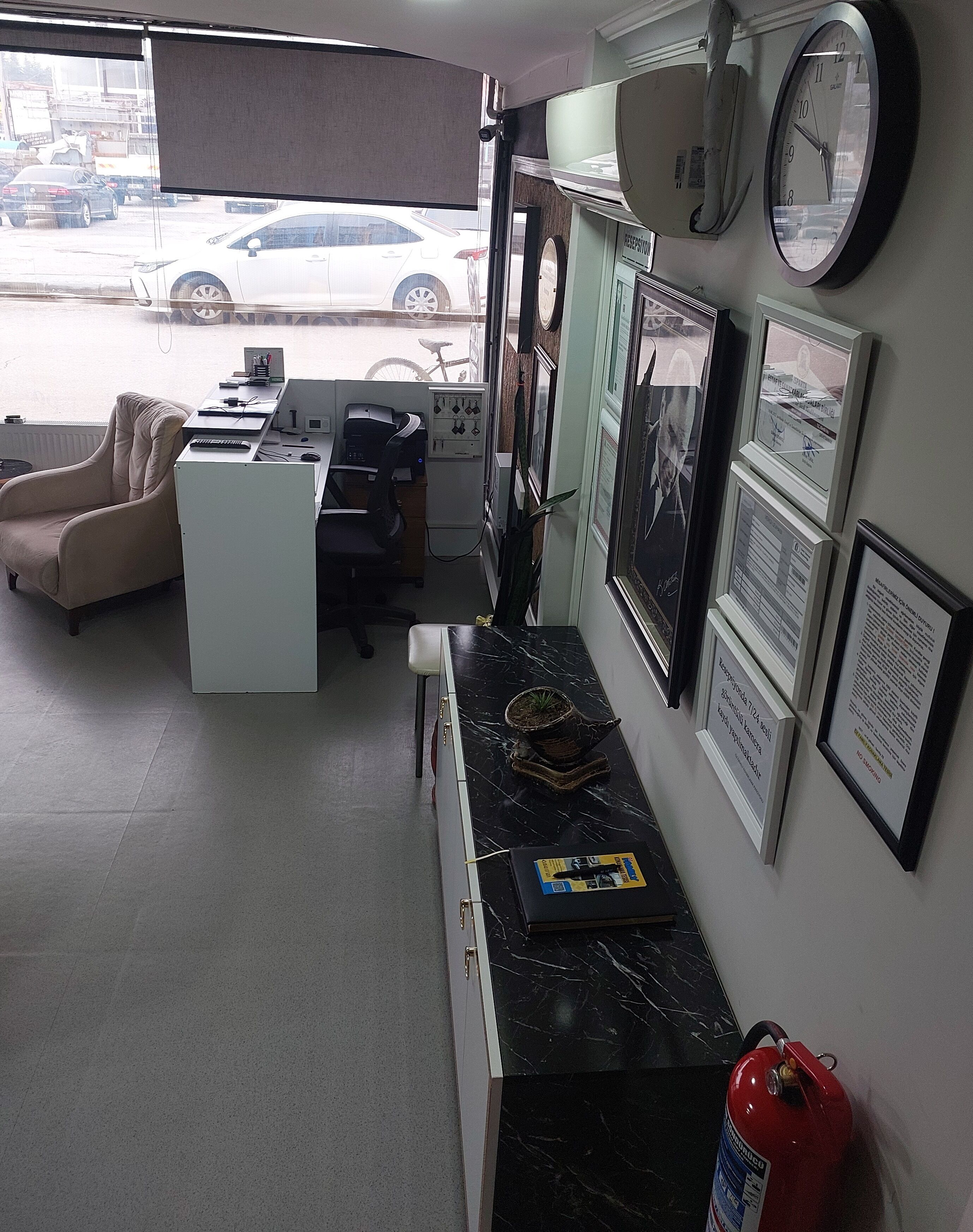 A room with a desk, chair, sofa, and a fire extinguisher.